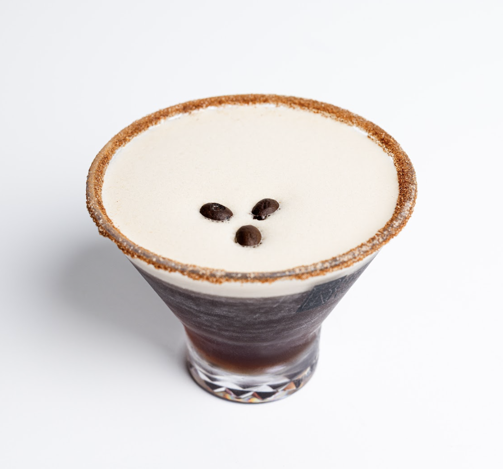 A creamy espresso martini from the Menu in a glass rimmed with brown sugar, topped with three coffee beans, set against a white background.