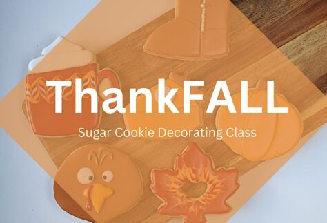 Four fall-themed sugar cookies (a boot, mug, turkey, and maple leaf) are displayed on a wooden board with the text ThankFALL Sugar Cookie Decorating Class overlayed in a translucent orange diamond.