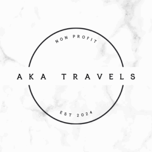 A circular logo with the words AKA TRAVELS in bold letters across the center, NON PROFIT at the top, Benefiting Vets for Youth, and EST 2024 at the bottom, set on a light marble background.