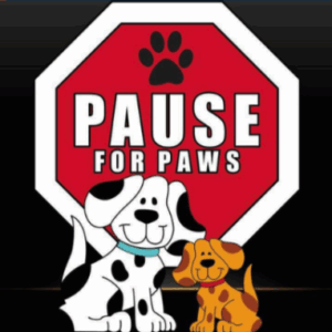 Two cartoon dogs sit in front of a red stop sign featuring a black paw print and the words Pause for Paws. The background is black, and the sign suggests taking time for pets.