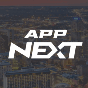 City skyline at dusk with illuminated buildings and streets. The bold white text APP NEXT is centered over the image, partially obscuring the city view in the background.