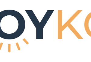 Logo reading JOY KC with JOY in dark blue and KC in orange. The O in JOY features yellow rays below it, resembling a rising sun. White background. Design celebrates Giveback Benefiting Vets for Youth.