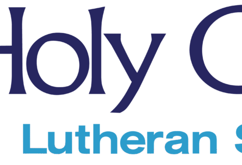 Logo for Holy Cross Lutheran School featuring a blue cross, with large text spelling Holy Cross Lutheran School to the right, highlighting a Giveback Benefiting Vets for Youth initiative.