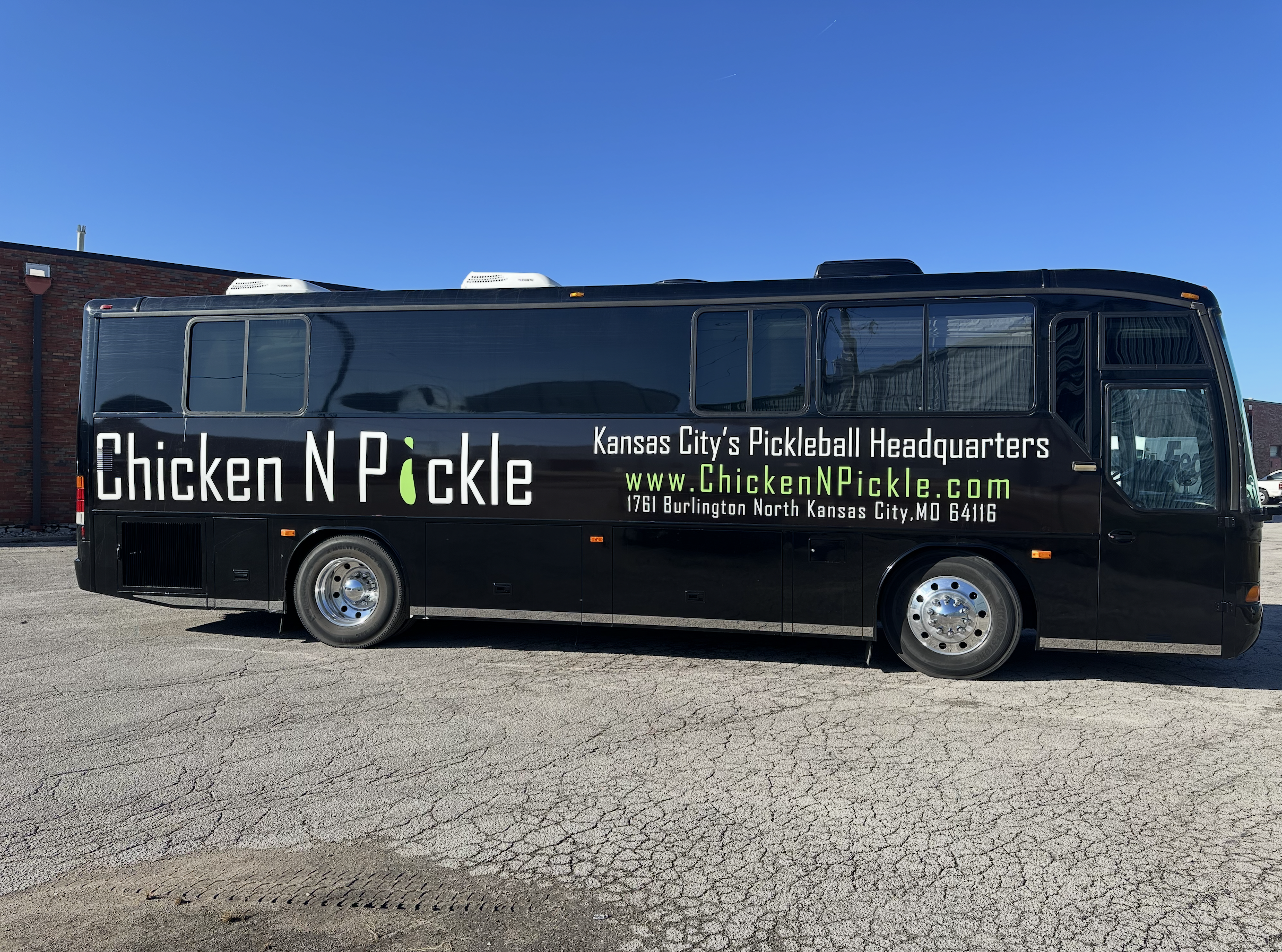 A black bus with Chicken N Pickle and Kansas Citys Pickleball Headquarters written on the side, along with the website www.ChickenNPickle.com and the address 1761 Burlington North Kansas City, MO 64116.
