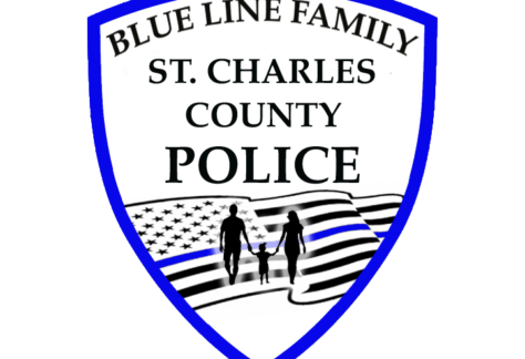 A police badge with a blue outline reads Blue Line Family St. Charles County Police above an American flag with a blue stripe and silhouettes of two adults and a child holding hands, highlighting a Giveback Benefiting Vets for Youth.