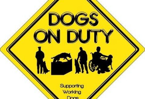 Yellow diamond-shaped sign with DOGS ON DUTY in bold black letters, silhouettes of dogs and handlers, including a wheelchair user, and text Supporting Working Dogs underneath. Perfect for your 10% Giveback Night Benefiting HEAL Center for the Arts at Chicken N Pickle.