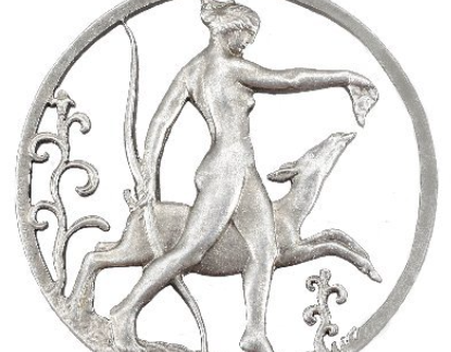 A silver medallion showing a nude woman holding a bow and leading a deer by the neck, with ornate floral designs framing the scene.