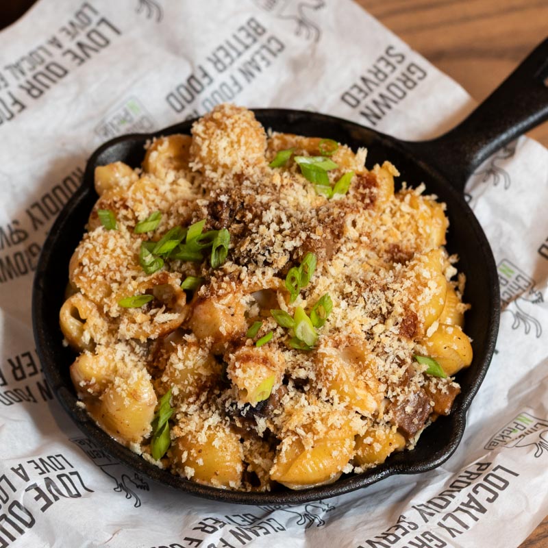 A cast iron skillet filled with baked macaroni and cheese topped with breadcrumbs and chopped green onions, resting on branded parchment paper.